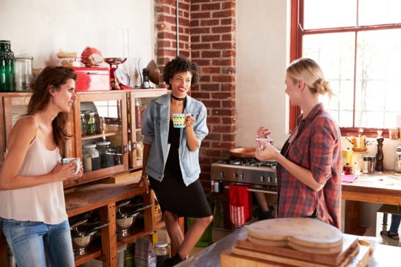Three young adult girlfriends talk over coffee in kitchen